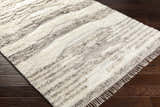 Close-up of the hand woven Kingsthorpe Area Rug. Cream, taupe, and dark brown shag rug with fringe on dark wood floors. Corner