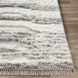 Close up of the hand woven Kingsthorpe Area Rug showing cream, taupe and dark brown shag stripes and fringe detail. Front