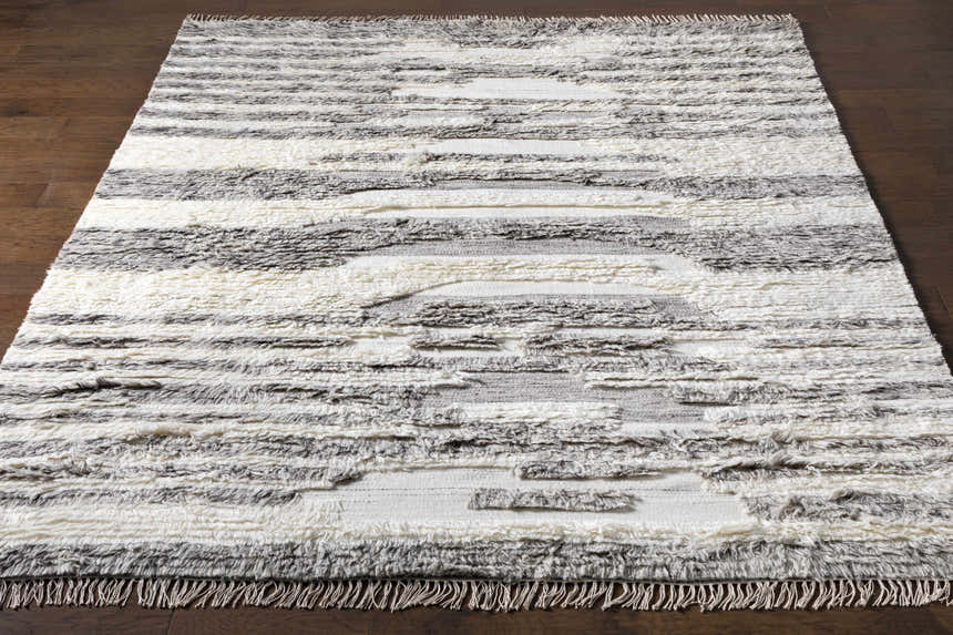 Close-up of the hand woven Kingsthorpe Area Rug. Cream, taupe, and dark brown wool shag rug with horizontal stripes and fringe. Front