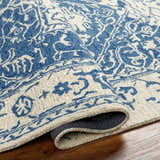 Close-up of the hand-tufted Koppies Area Rug in bone and denim. Features a traditional floral pattern and wool texture. Fold