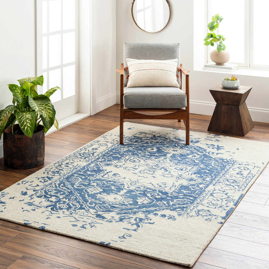Living room scene with Koppies Area Rug in bone and denim, gray chair, wood accents, and natural light. Roomscene-Rectangle