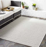 Styled patio with a Kirkburton Beige Outdoor Rug, charcoal wicker sofa, and white brick wall. Roomscene-Rectangle