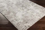 Close-up of the Kutloanong Area Rug showing its charcoal, gray, and ivory contemporary design on dark wood flooring. Corner
