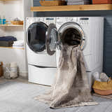 Laundry room scene with Kuyucak Washable Area Rug coming out of the washing machine. Gray, brown, and cream colors. Washing-Machine