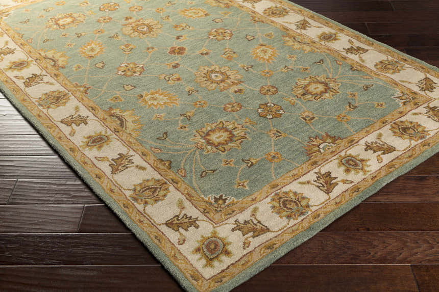 Close-up of a Lagrange Sage Regency Wool Carpet with floral pattern and beige border on dark wood floor. Corner