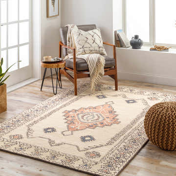 Living room scene with a Laketon Wool Area Rug in charcoal, dusty pink, and ivory, styled with a leather chair and pouf. Roomscene-Rectangle