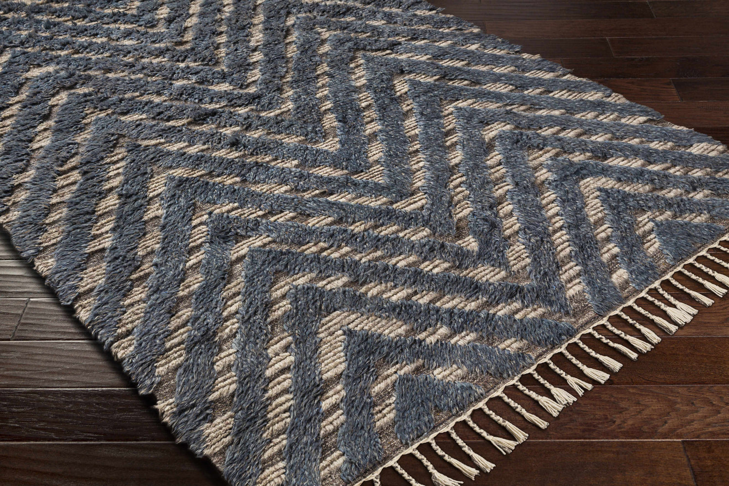 Close-up of the Lambsburg Knotted Wool Rug. Blue and light beige zig-zag pattern with fringe on dark wood floor. Corner