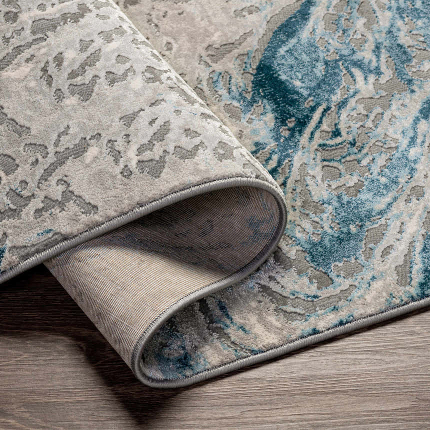 Close-up of the Lambton Blue Marble Area Rug showing its charcoal, cream, and teal abstract pattern and woven texture. Fold