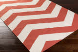 Close-up of the Lapeer Area Rug. Beige and rose wool rug with a bold, contemporary chevron pattern. Hand woven texture. Corner