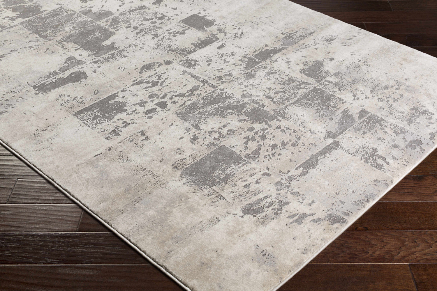 Close-up of the Lares Area Rug showcasing its charcoal, light beige, and gray contemporary pattern on dark wood floors. Corner
