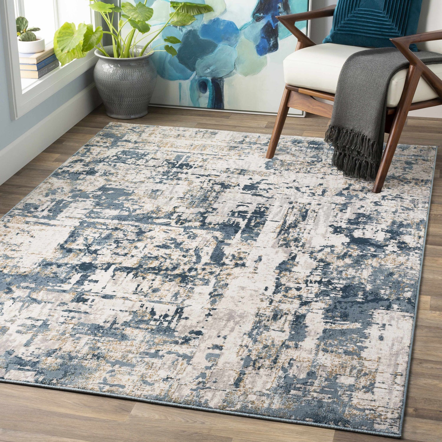 Living room scene with a Larne Area Rug in dark blue, gray, and beige, styled under a chair with a throw and pillow. Roomscene-Rectangle