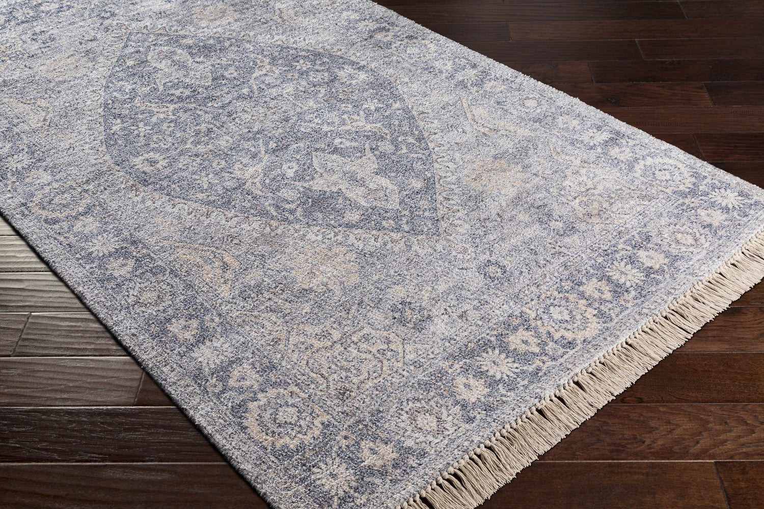 Close-up of the Laura Area Carpet, a beige and blue hand-woven rug with a traditional design and fringe detail. Corner
