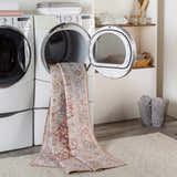 Laundry room scene with Cream Rust Leeston Washable Rug coming out of dryer. Bohemian vintage style rug in brick red, cream, and blue. Washing-Machine