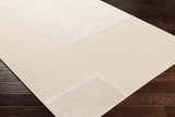 Close-up of the Lice Area Rug showing its textured, grid-like pattern in a soft, neutral cream color on dark wood flooring. Corner