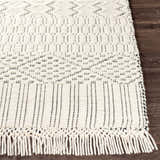 Close-up of the hand-woven Limoges Area Carpet. Cream wool rug with black geometric pattern and fringe on dark wood floor. Front