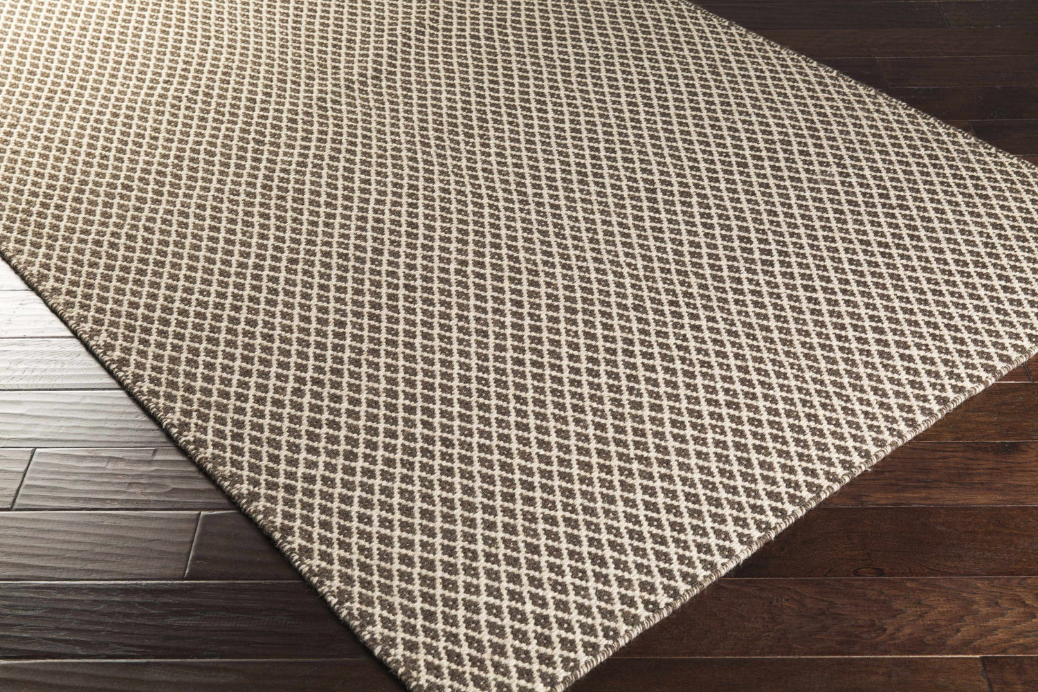 Close up of Lingo Brown Trellis Flatweave Rug showing dark brown and oatmeal diamond pattern on dark wood floor. Corner
