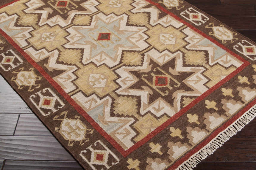 Close-up of the hand woven Liscomb Area Rug. Brown, ivory, mustard, and pale blue geometric pattern. Wool texture. Corner