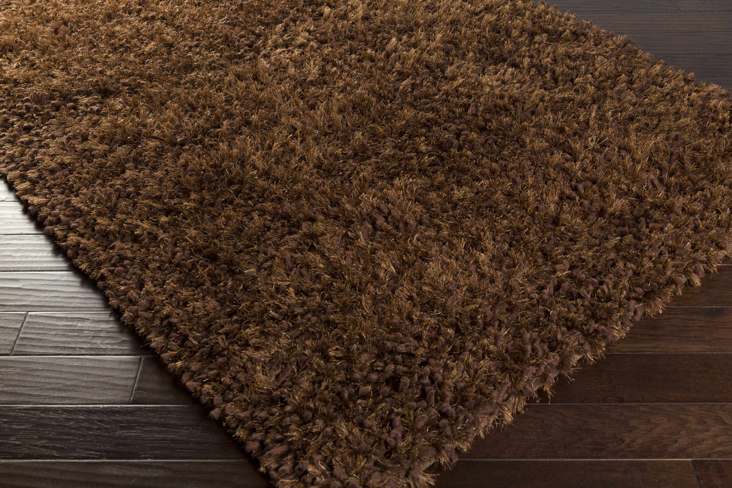 Close-up of the dark brown, shag Lizton Area Rug on dark wood floors. Wool and polyester blend. Corner