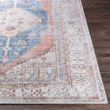 Close-up of the Lake Area Rug showing its bohemian-inspired pattern in navy, coral, tan, and light gray on a dark wood floor. Front