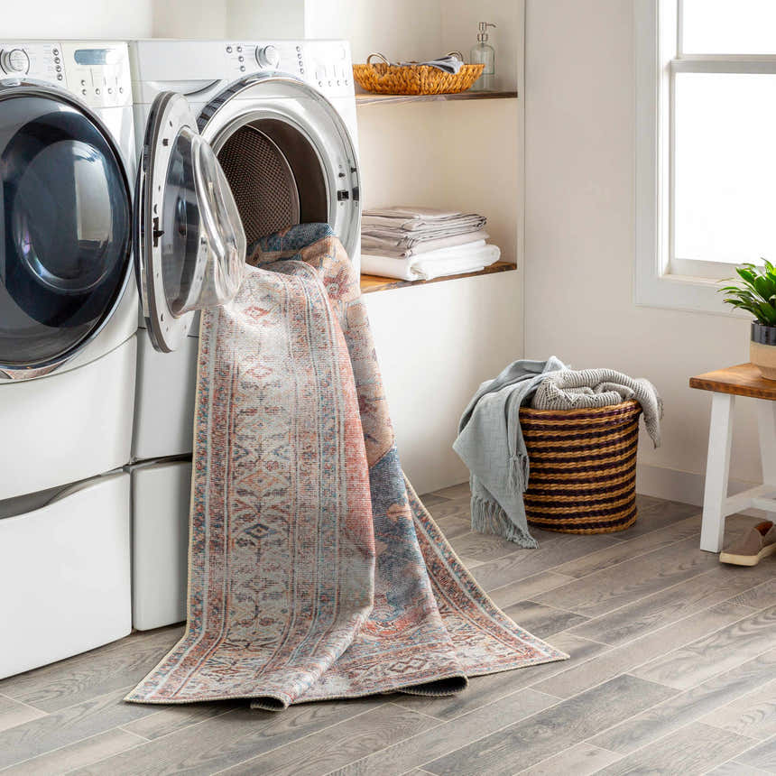 Laundry room scene with Lake Area Rug partially inside the washing machine. Bohemian style rug with coral, blue and tan colors. Washing-Machine