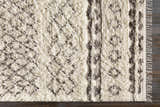 Close-up of the Lochwinnoch Area Rug. Beige shag rug with a dark brown Moroccan-inspired pattern and hand-woven fringe. Corner