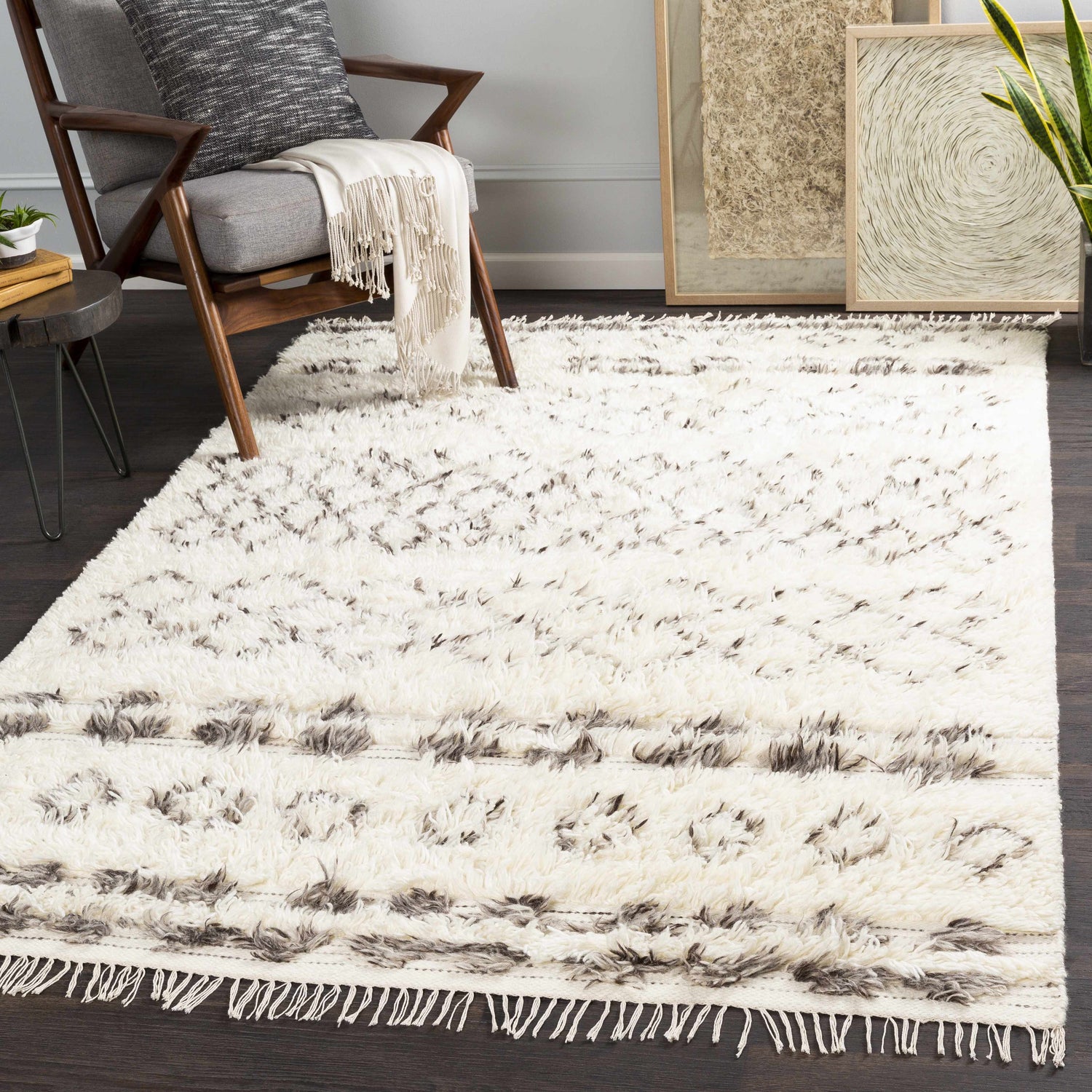 Living room scene with a beige Lochwinnoch Area Rug, gray chair, wood accents, and neutral wall art. Roomscene-Rectangle