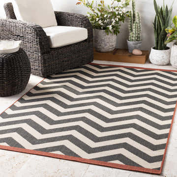 Outdoor patio scene with black wicker furniture and the Lockhart Outdoor Rug in a bold black and light beige chevron pattern. Roomscene-Rectangle