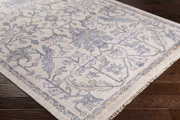 Close-up of the hand-knotted Loleta Area Rug. Beige viscose rug with charcoal, dusty pink, and light beige floral pattern. Corner