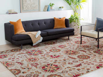 Living room scene with a Longford Beige Floral rug, gray sofa with orange pillows, and a modern chair. Roomscene-Rectangle