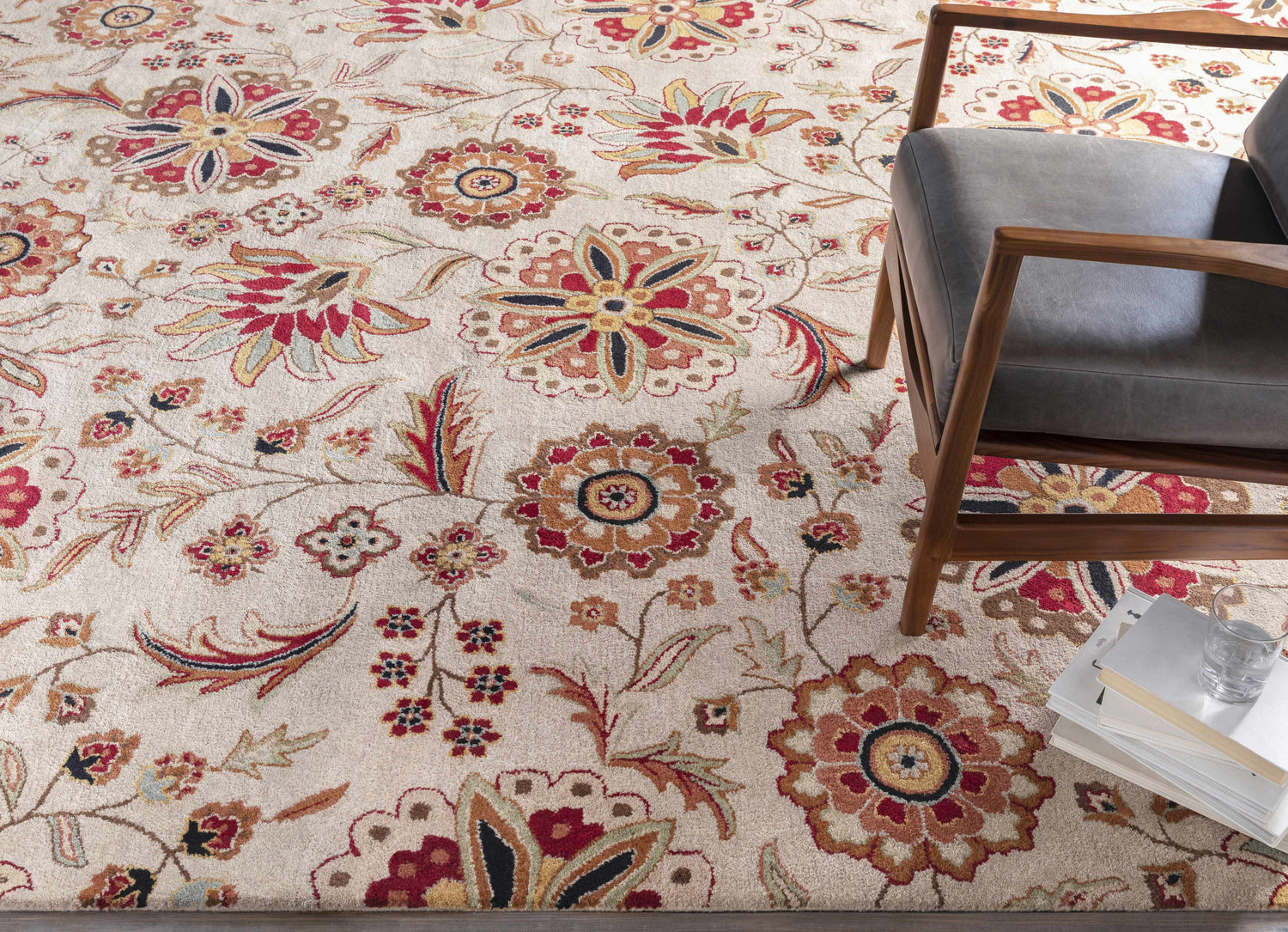 Room scene with a Longford Beige Floral rug, gray chair, and books. Traditional style. Styleshot