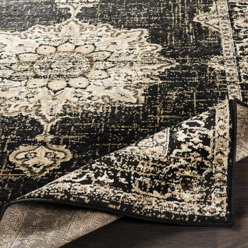 Close-up of the Lostwithiel Black Medallion Rug. Features a distressed black and beige traditional pattern. Fold