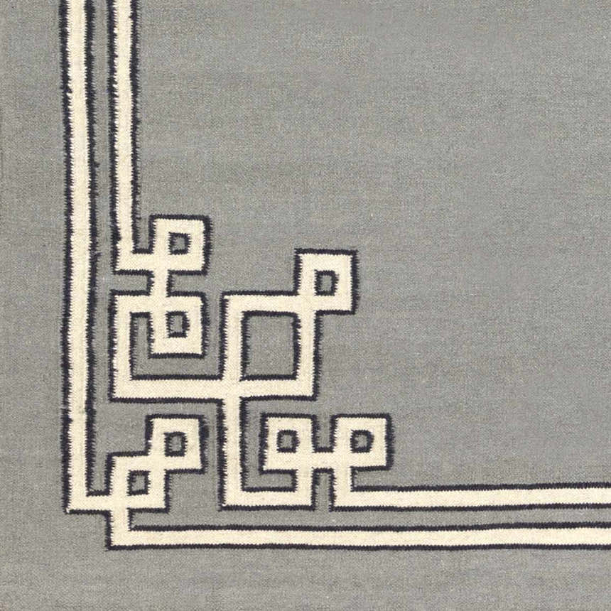Close up of the Lott Area Rug. Gray wool rug with an ink blue and light gray geometric border pattern. Swatch