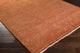 Close-up of the hand-knotted Lottsburg Premium Orange Wool Rug with a traditional floral and geometric pattern on dark wood floors. Corner