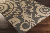 Close-up of the Loughton Area Rug, showcasing its black and light brown floral and damask pattern on dark wood floors. Corner