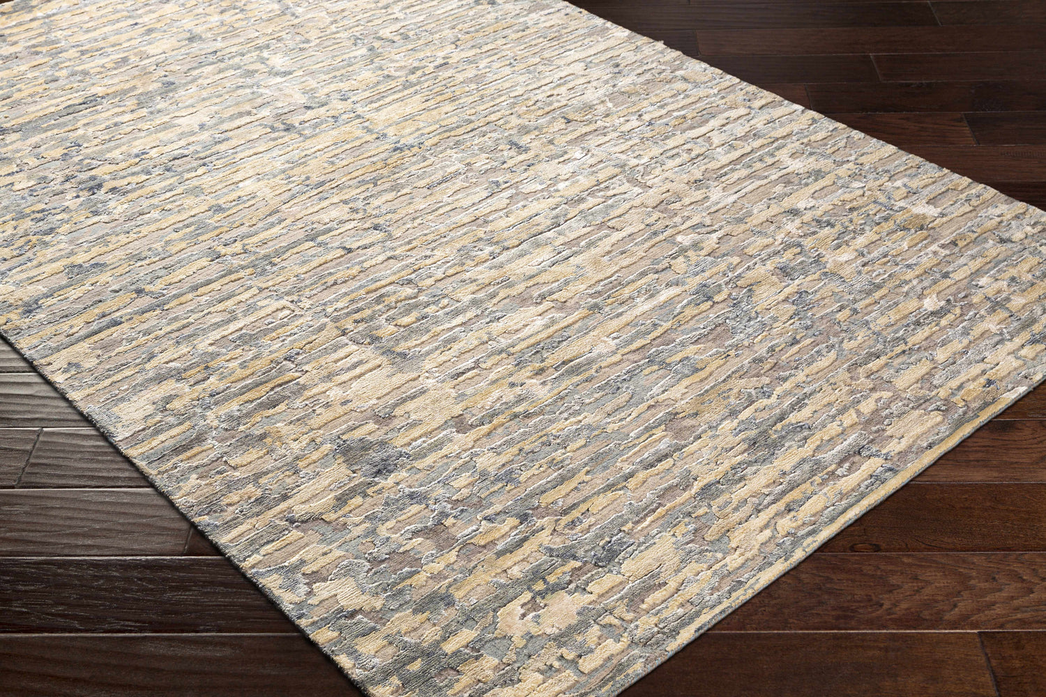 Close-up of the Lowdham Premium Rug, a hand-knotted rug in cream, beige, gray, and black on a dark wood floor. Corner