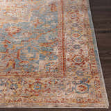Close-up of the Lumpkin Area Rug showing its traditional design, brick red, teal, and beige colors on dark wood flooring. Front