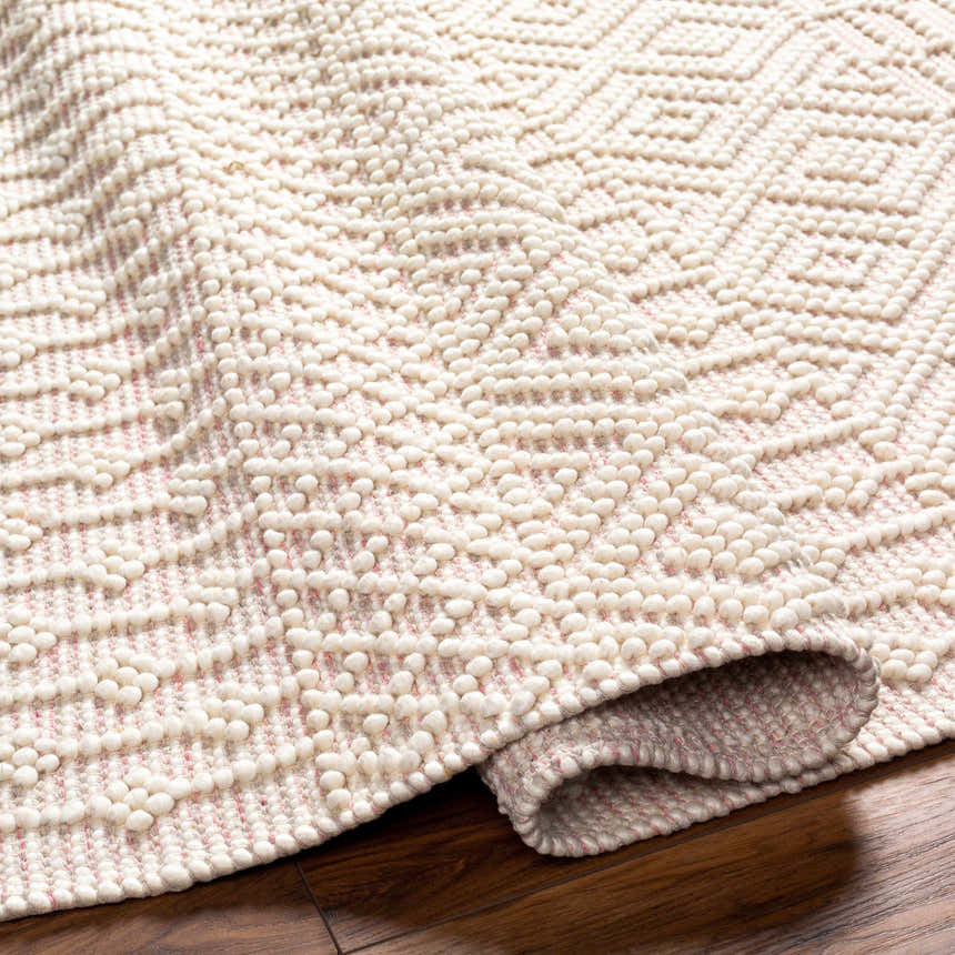 Close-up of the Luyu Area Rug. Hand-woven rug with cloud gray and light peach geometric pattern and raised, textured dots. Fold