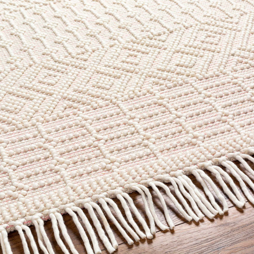 Close-up of the hand-woven Luyu Area Rug. Features a geometric pattern, cloud gray and light peach tones, and fringe detail. Texture