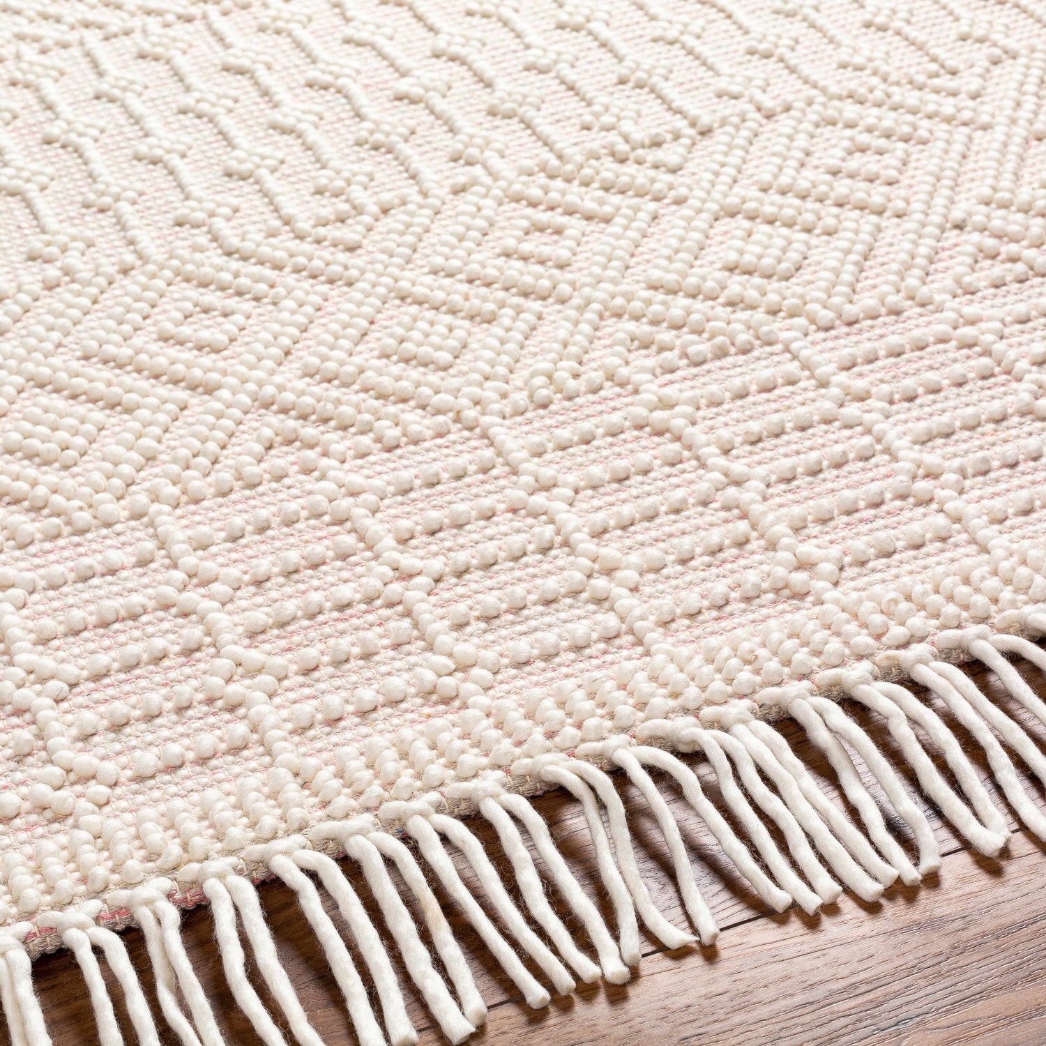 Close-up of the hand-woven Luyu Area Rug. Features a geometric pattern, cloud gray and light peach tones, and fringe detail. Texture