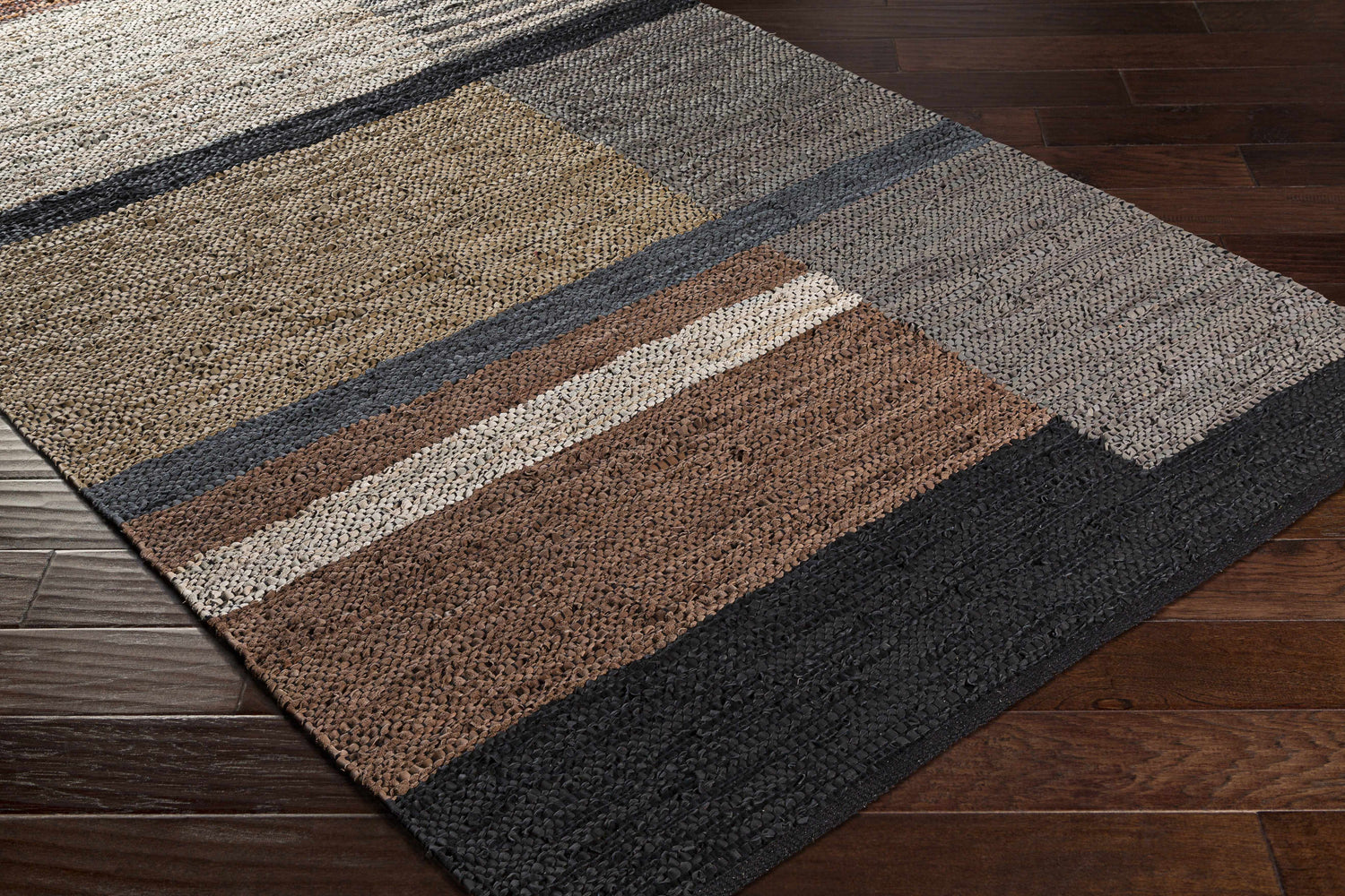 Close-up of the Lyndoch Leather Patchwork Rug. Features black, brown, and gray leather patches on a dark wood floor. Corner
