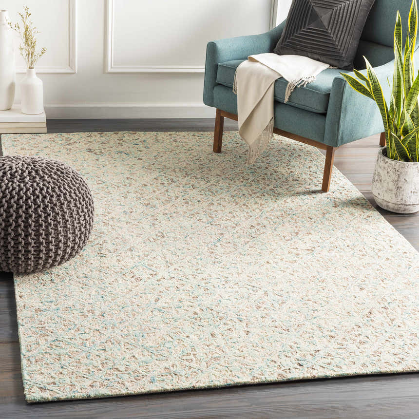 Living room scene with a Lysander Area Rug in light beige, blue, and brown, styled with a teal chair and gray pouf. Roomscene-Rectangle