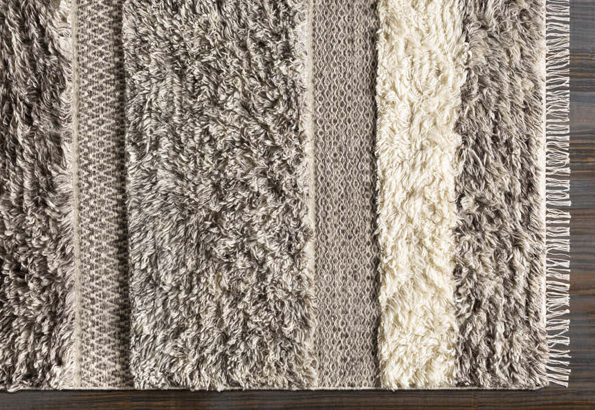 Close up of the hand woven Elizabeth Area Rug. Beige, dark brown, gray, and taupe shag rug with geometric pattern. Corner