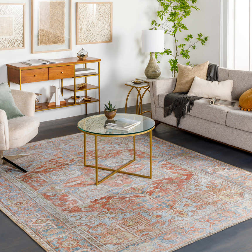 Living room scene with a Rust Maayon Washable Rug, sofa, chair, and gold accents. Bohemian style with brick red, blue, and brown tones. Roomscene-Rectangle