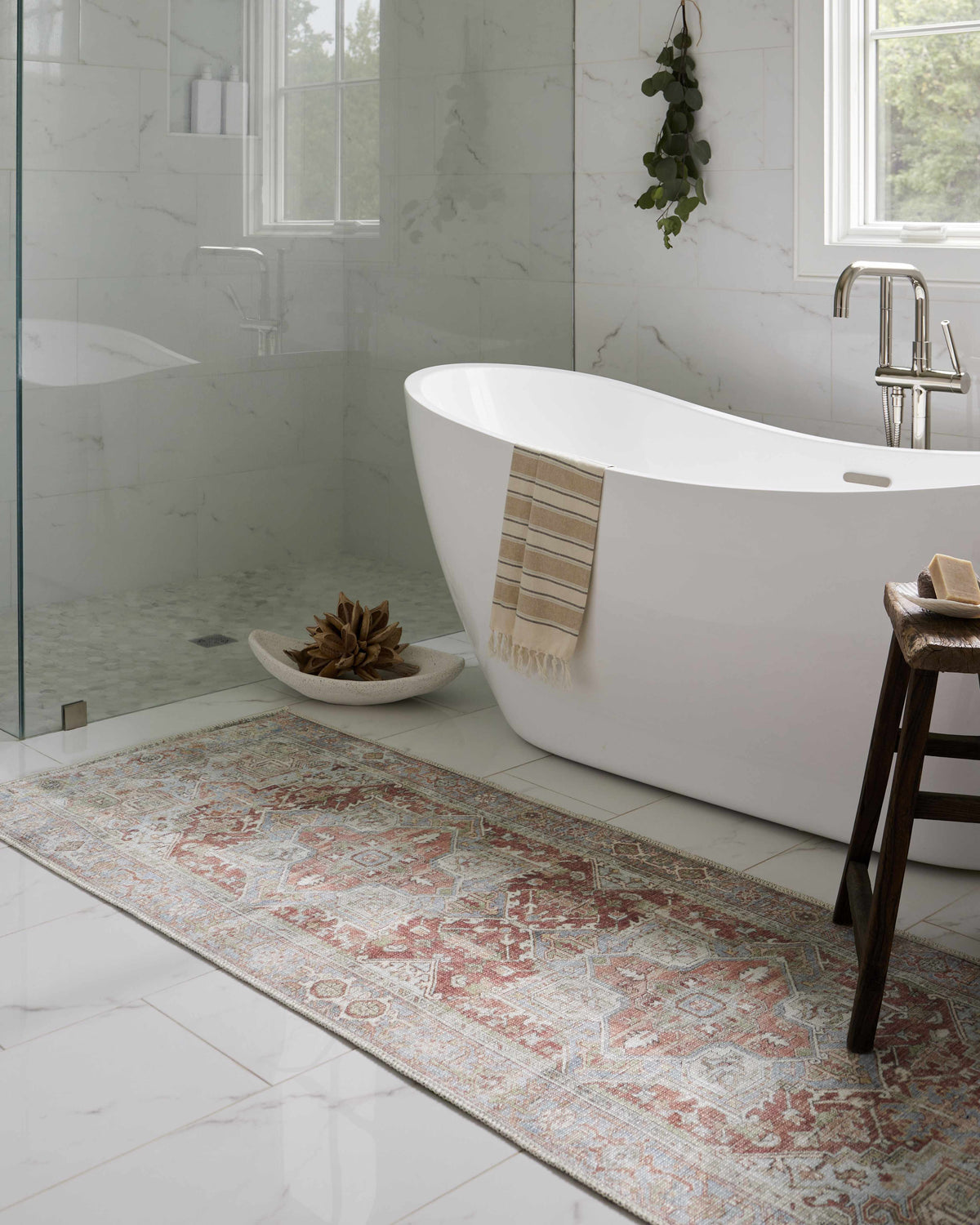 Bathroom scene with a white tub and Rust Maayon Washable Rug in brick red, brown, and blue on white marble tile floor. Roomscene-Runner