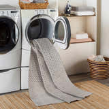 Laundry room scene with gray Maanas Washable Area Rug coming out of dryer, layered on a jute rug. Washing-Machine