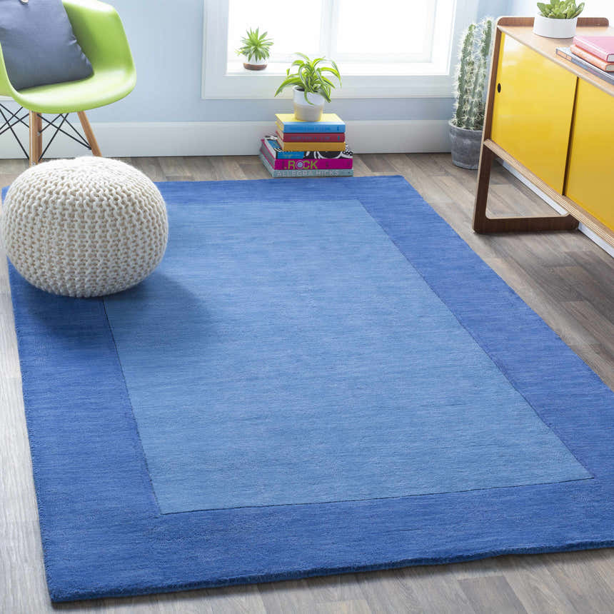 Bright room scene with a Macedon Blue Bordered Wool Rug, white pouf, lime green chair, and yellow cabinet. Roomscene-Rectangle