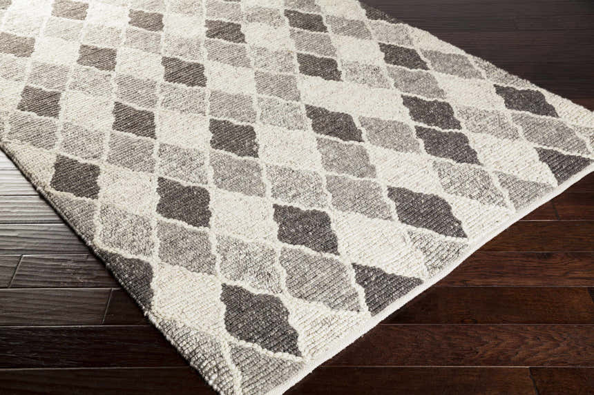 Close-up of Madden Premium Rug in black, charcoal, gray, and ivory with a diamond pattern on dark wood floors. Corner