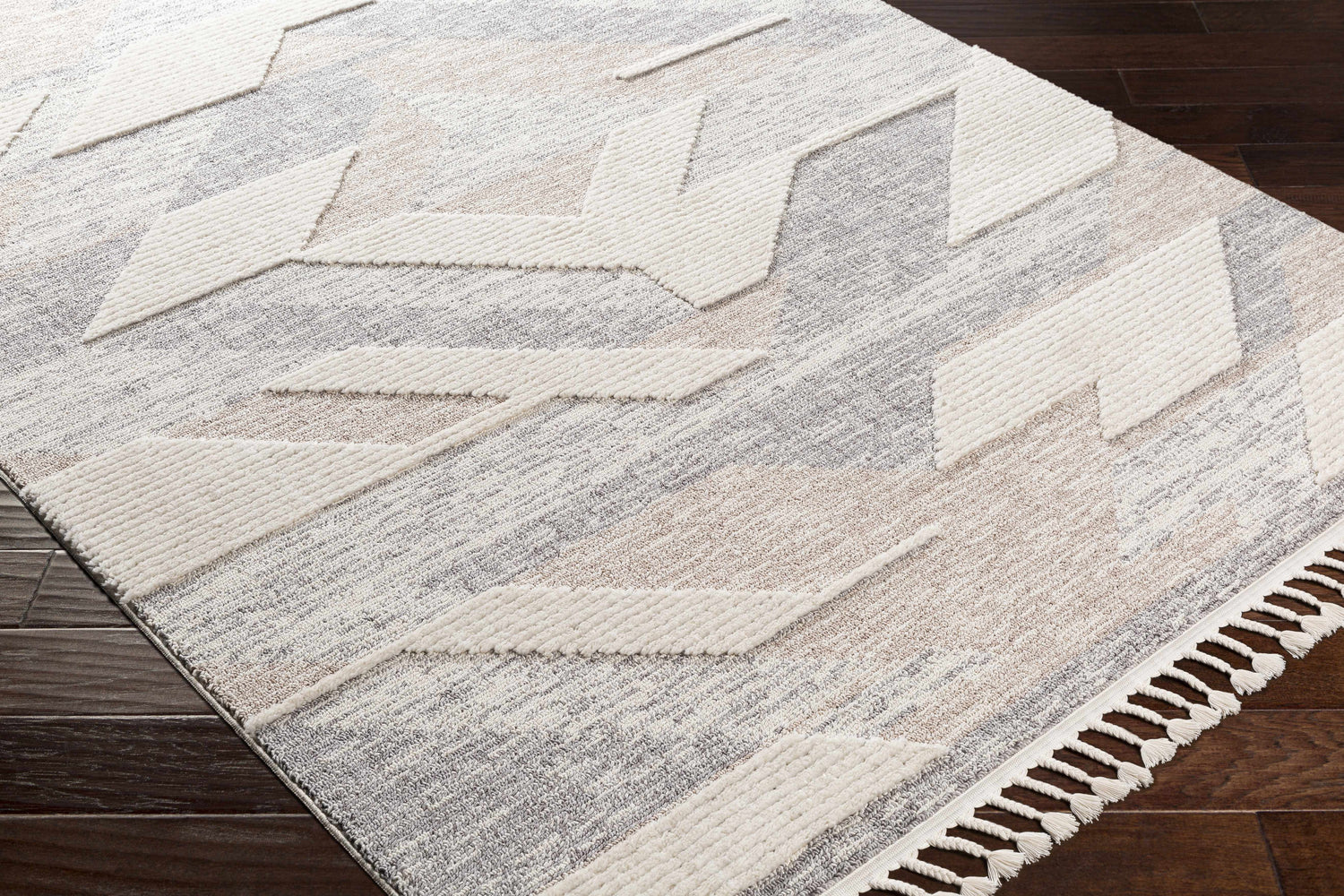 Close-up of the Magazine Geometric High/Low Pile Rug. Gray, tan rug with raised geometric pattern and tassels. Corner