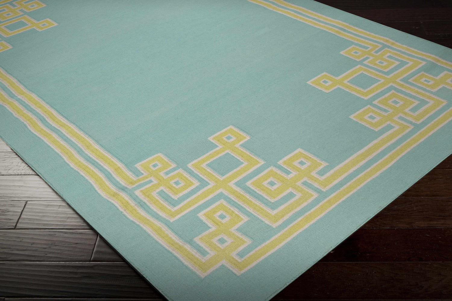 Close-up of the Manitou Area Rug, a contemporary hand-woven rug in aqua with a light olive geometric border. Corner