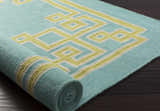 Close-up of a rolled Manitou Area Rug. Aqua wool rug with a geometric light olive and gray pattern. Hand woven texture. Styleshot